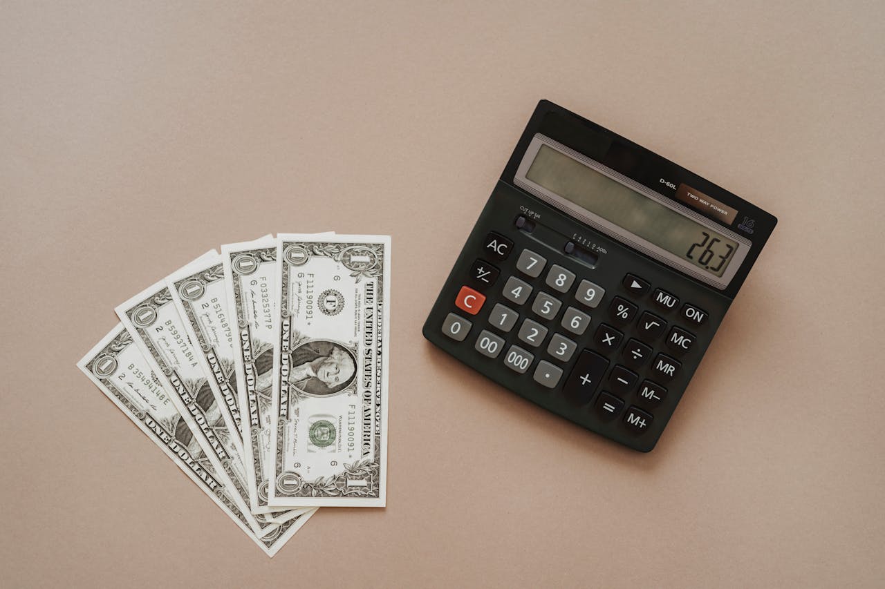 A calculator displaying 26.3 beside four one-dollar bills on a beige background.